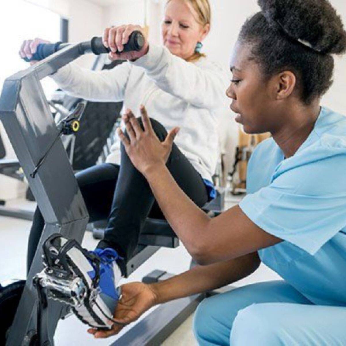 A therapist working setting up a patient on a recumbent stationary bicycle
